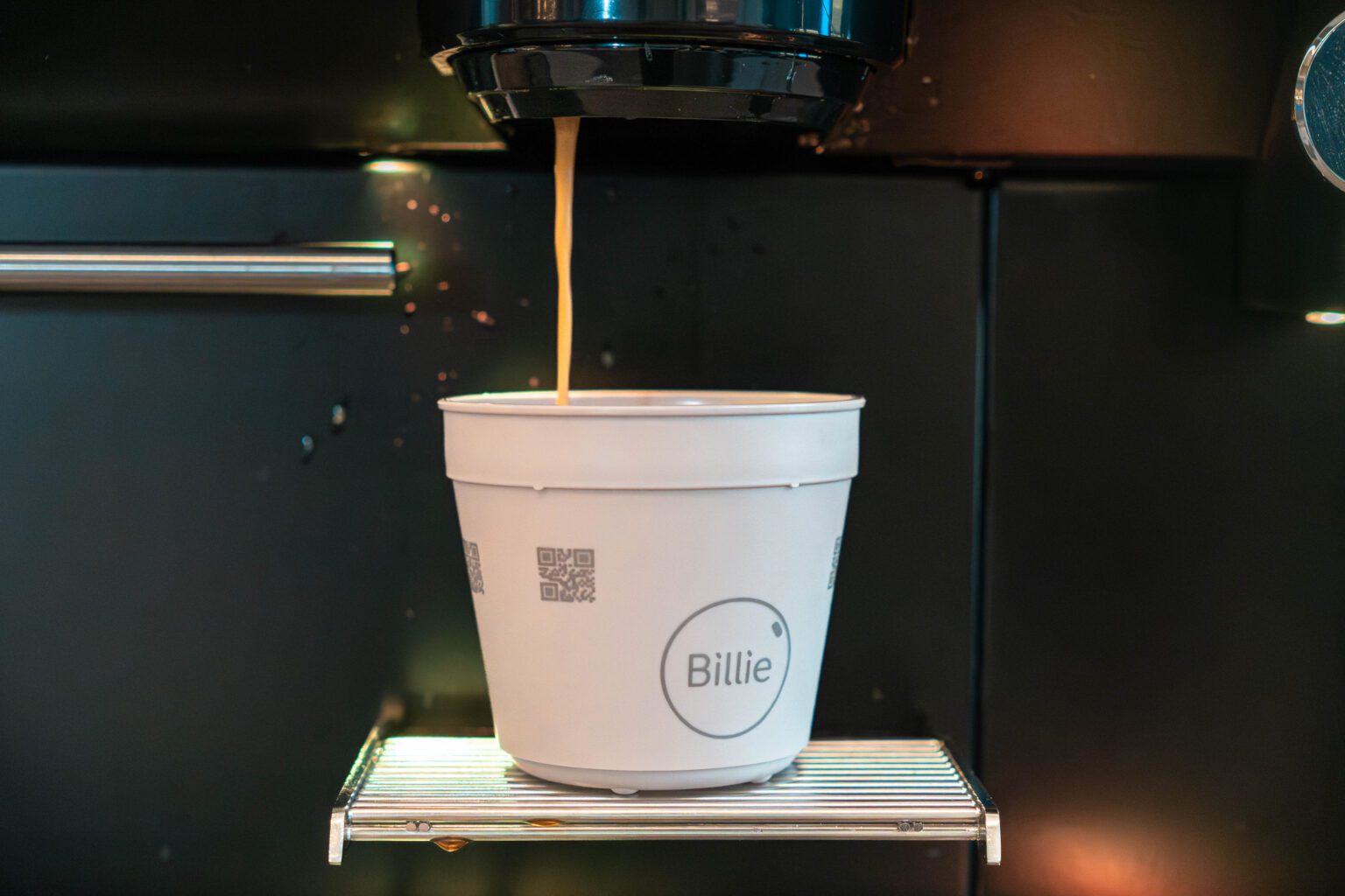 Democratisch koffie proeven: ‘Wat zuur en bitter achter in je gehemelte’ Close-up van een witte Billie cup. In de cup loopt een straaltje koffie uit de koffie-automaat.