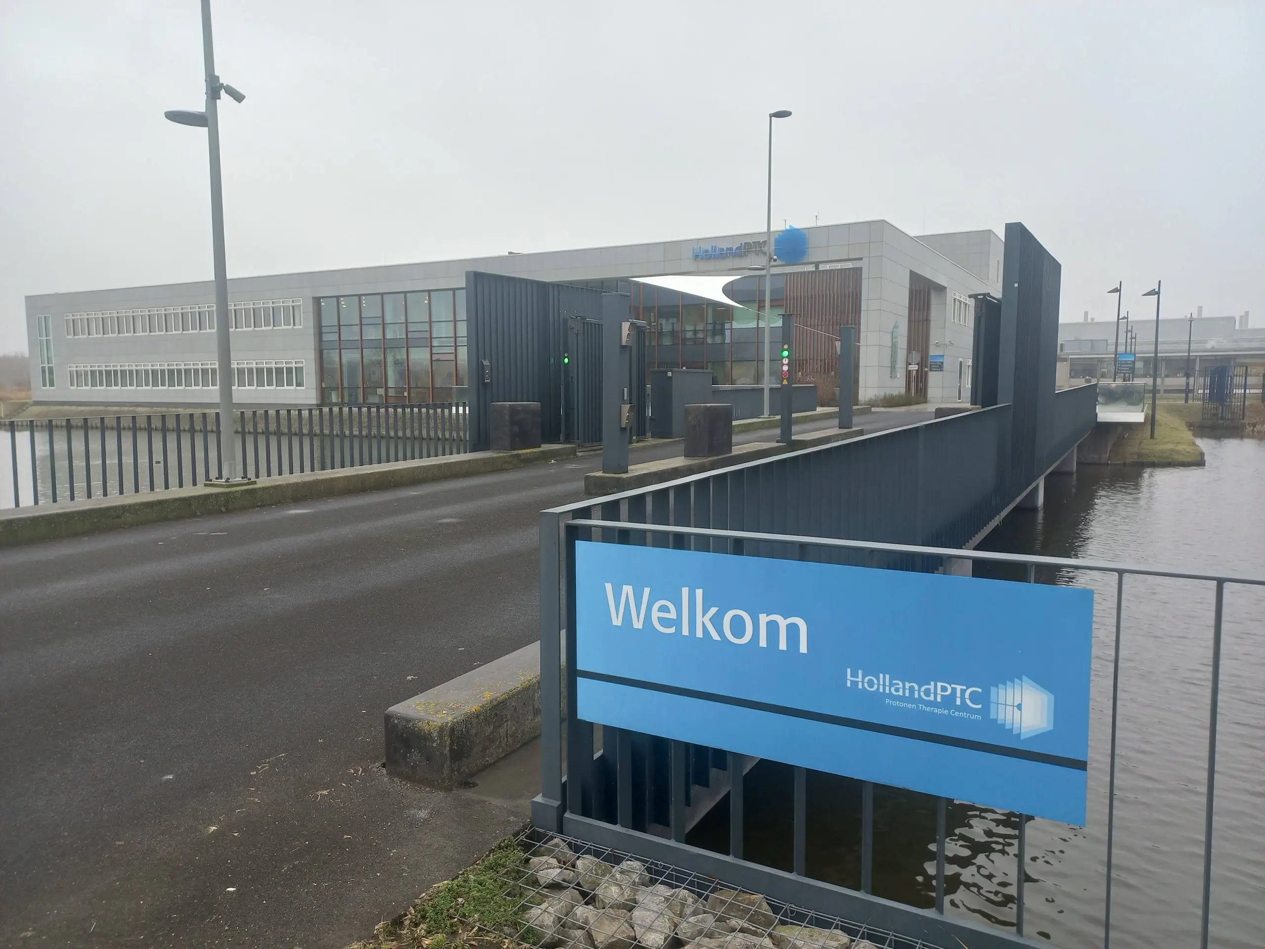 NRC newspaper: Against its better judgement, TU Delft continues to put money into proton clinic Het gebouw van Holland PTC met op de voorgrond een bord met "Welkom' erop