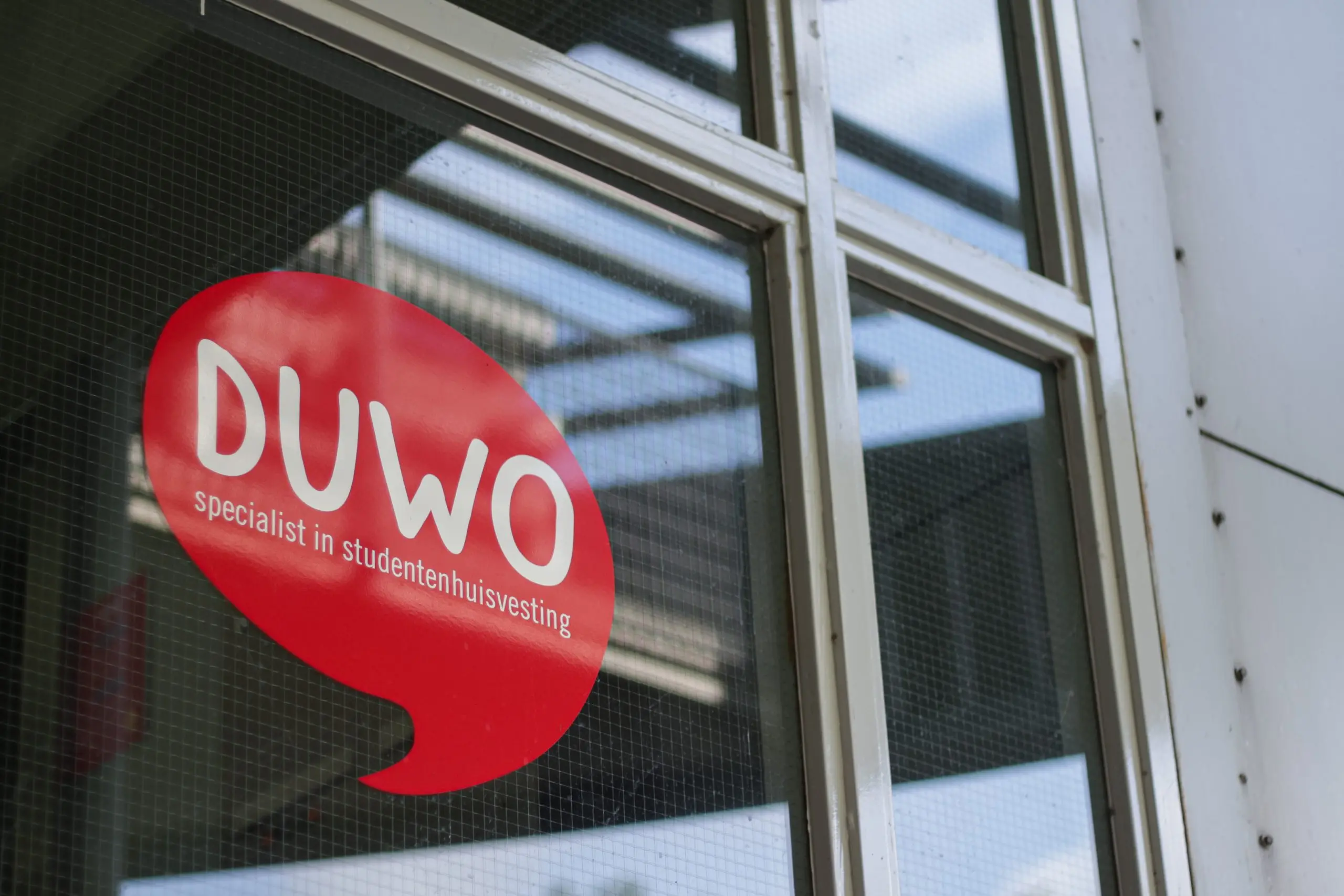 Het logo van studentenhuisvester Duwo op een raam. Het logo is rood, in de vorm van een tekstballon. In het midden staat 'Duwo'.