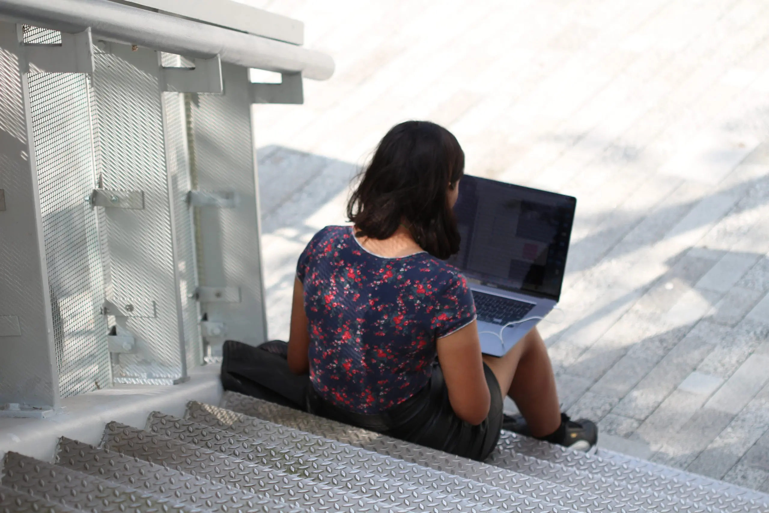 iemand zit buiten onderaan een trap te werken op haar laptop