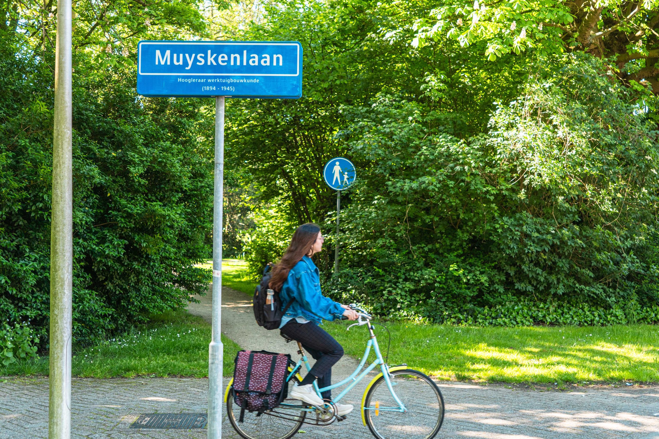 Iemand fietst langs een straatnaambordje van de Muyskenlaan.