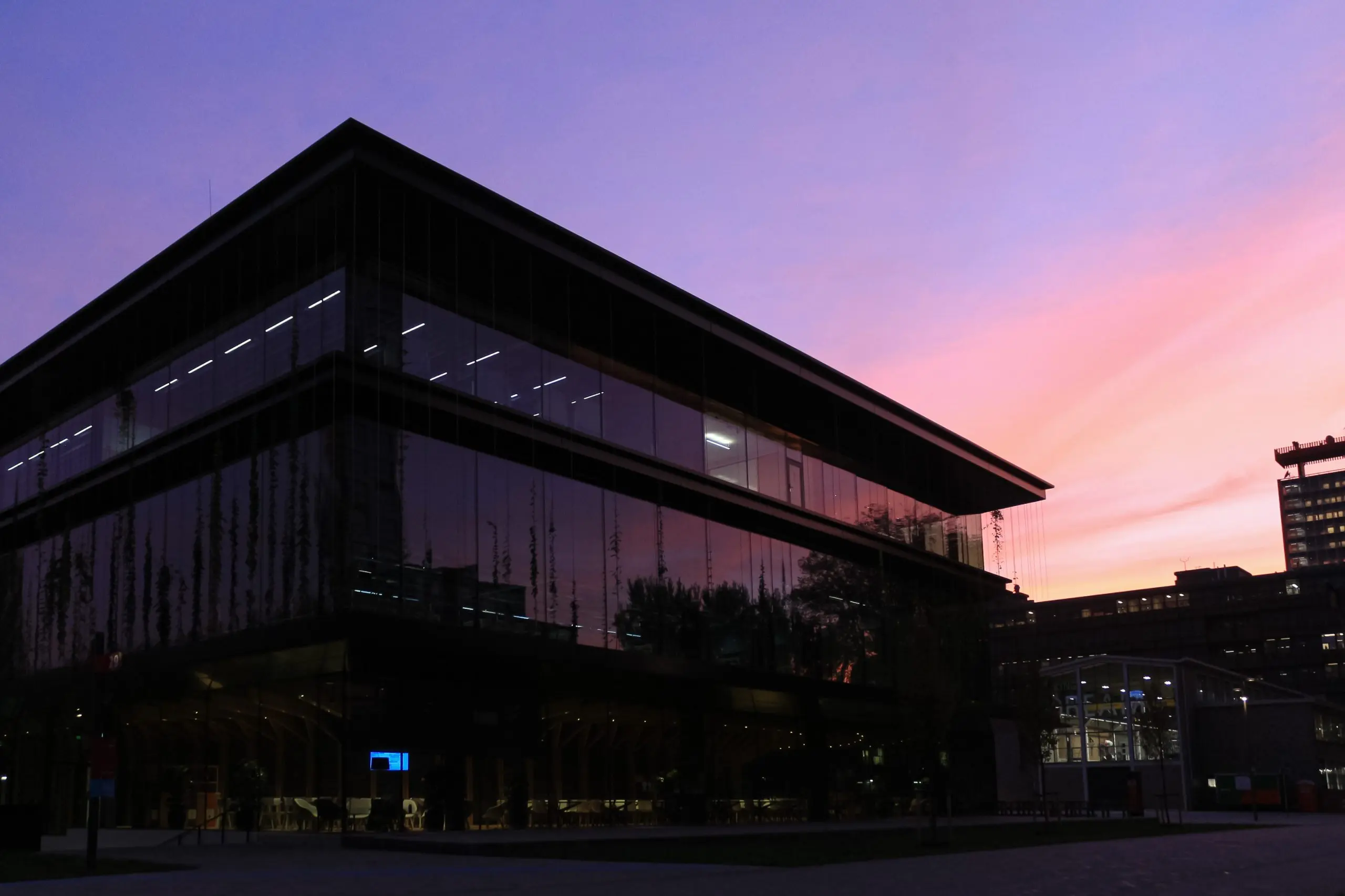 Een gebouw bij de ondergaande zon. De lucht kleurt paars en roze, het gebouw is bijna zwart