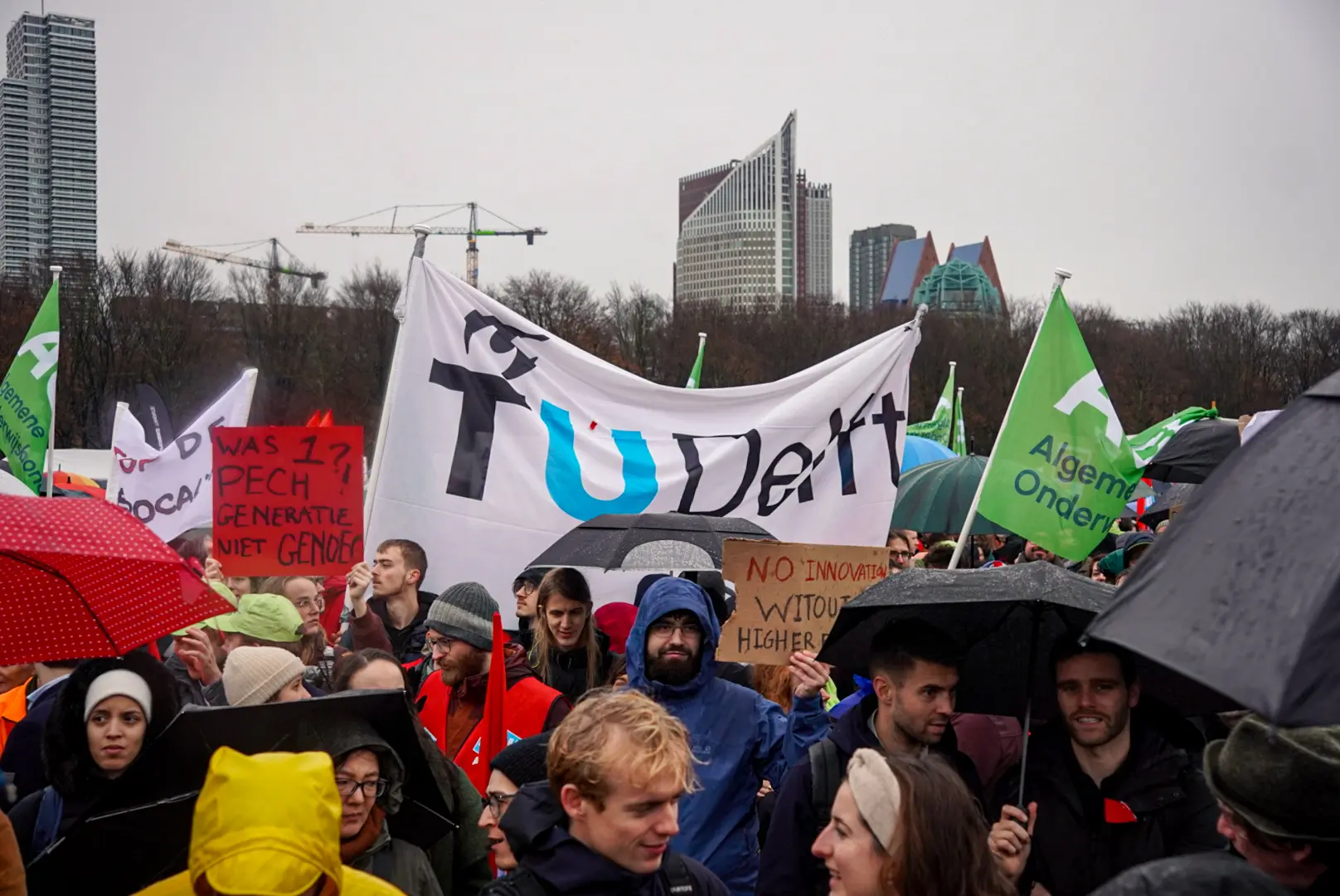 Mensen demonstreren. Ze hebben een grote banner van de TU Delft mee.