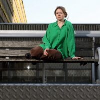 Jenna Pfeifer zit met opgetrokken benen buiten op een bankje, Ze poseert voor de foto