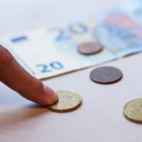 Een paar munten en een briefje van 20 euro liggen op tafel. Een vinger rust op 1 van de munten.