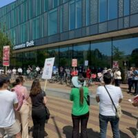 Mensen demonstreren voor het station Delft. Ze dragen borden tegen de oorlog in Iran
