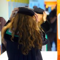 Een vrouw van achteren gezien, staat voor een spiegel en past een baret