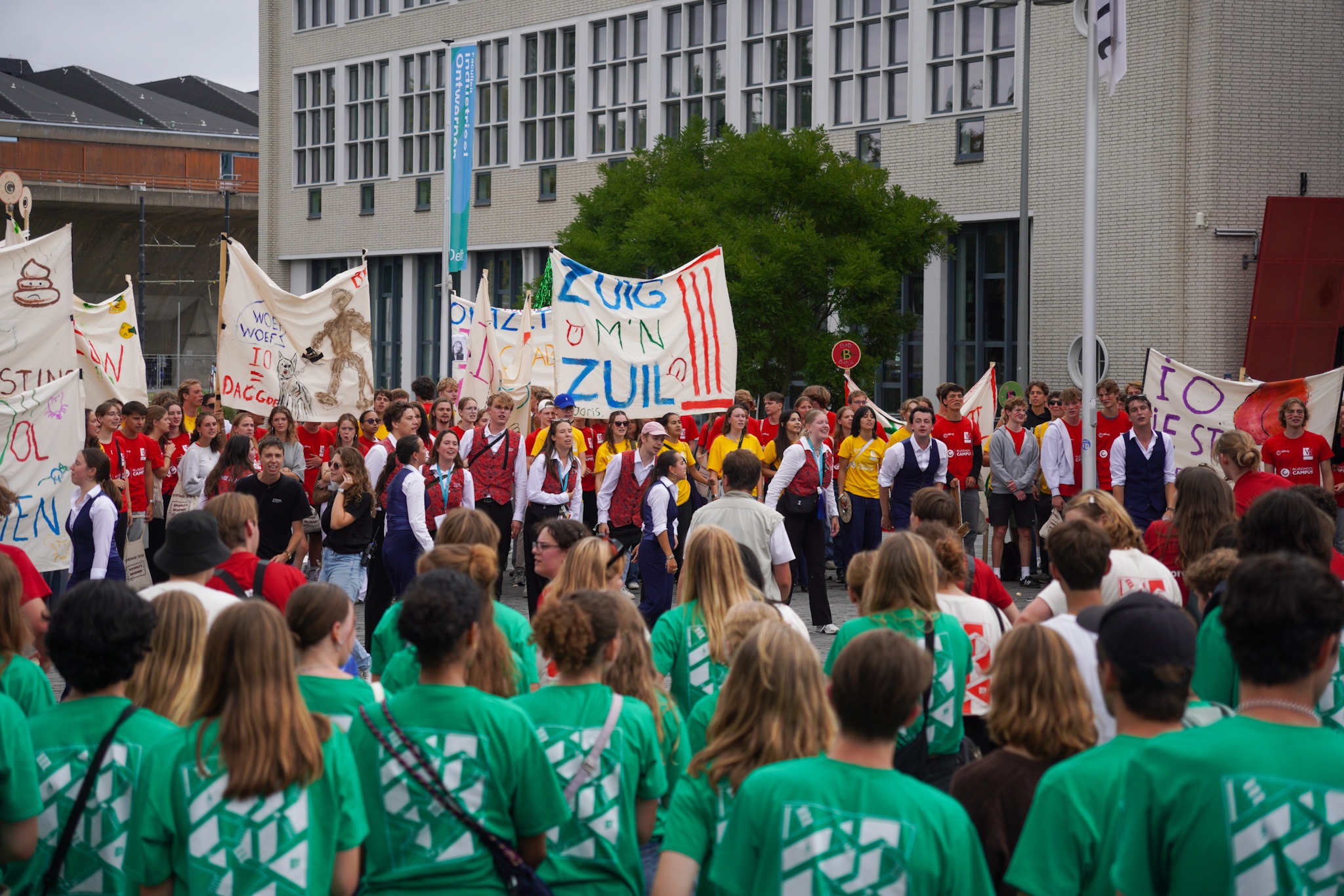 Studenten in groene shirts staan tegenover studenten in rode shirt. Die laatste groep draagt spandoeken mee.