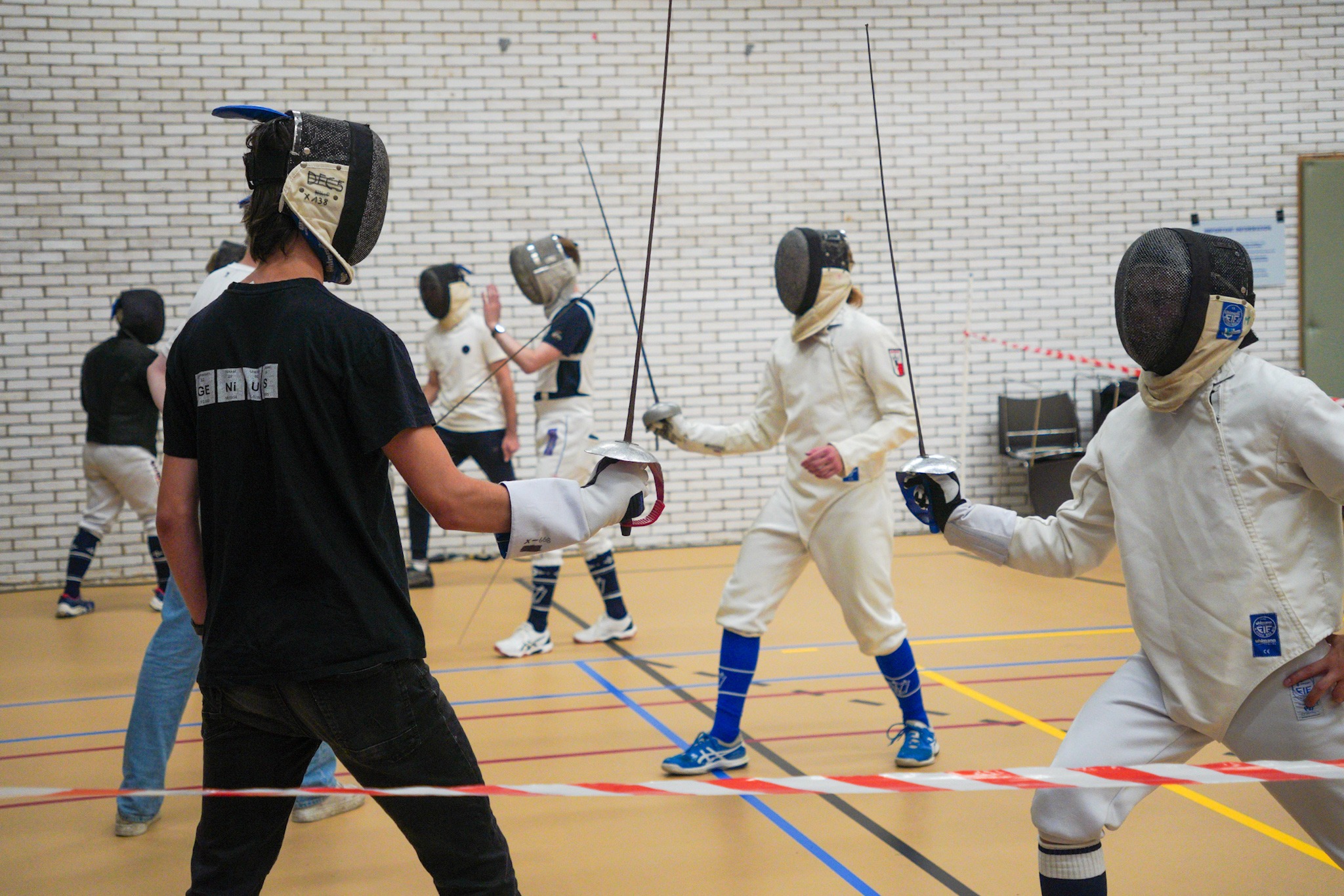 Studenten in schermpakken staan tegenover OWee-deelnemers met een schermhelm op en kruisen met hen de degens.