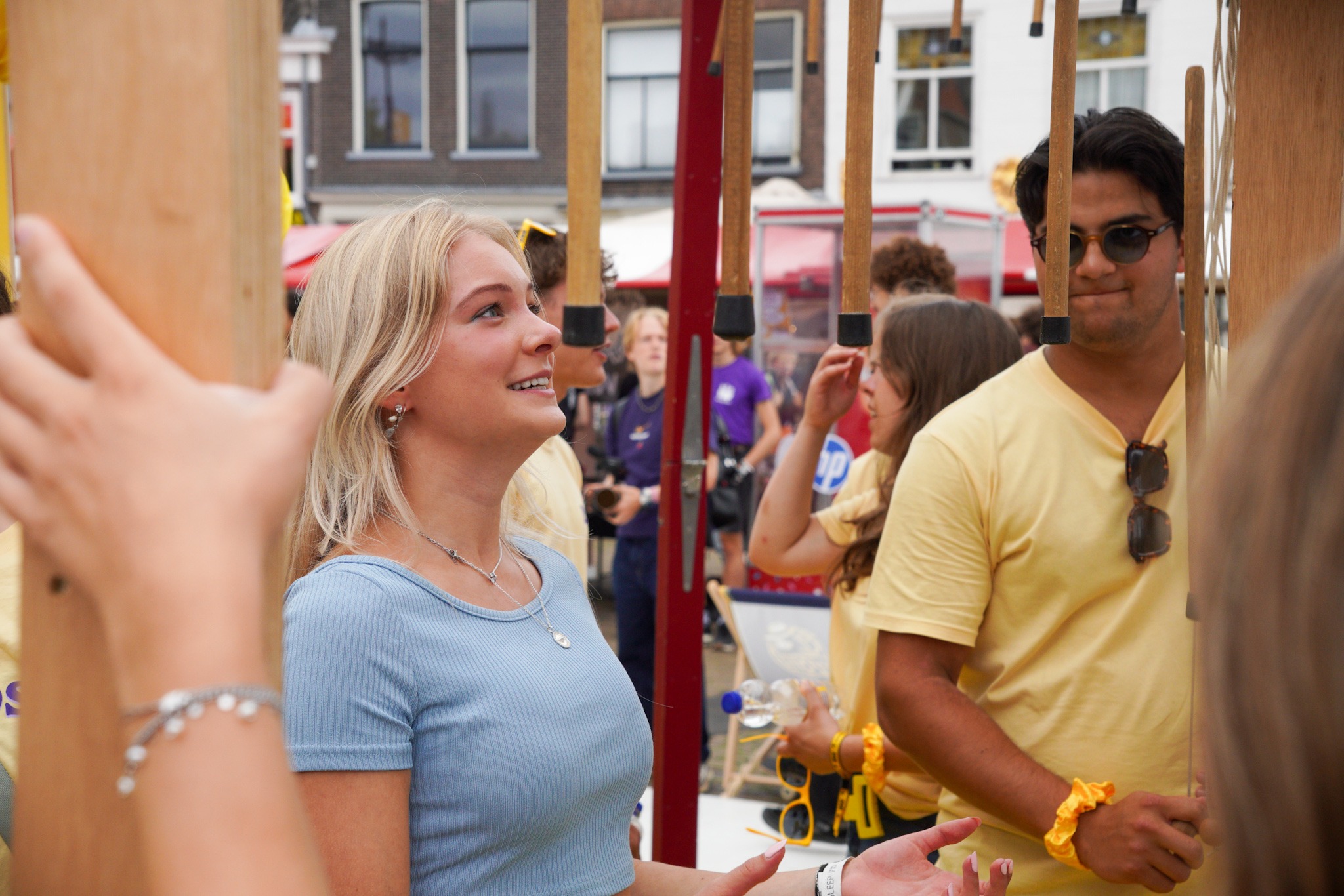 Een deelneemster kijkt op de infomarkt van de OWee geconcentreerd naar hangende, houten stokken. Een student kijkt toe.