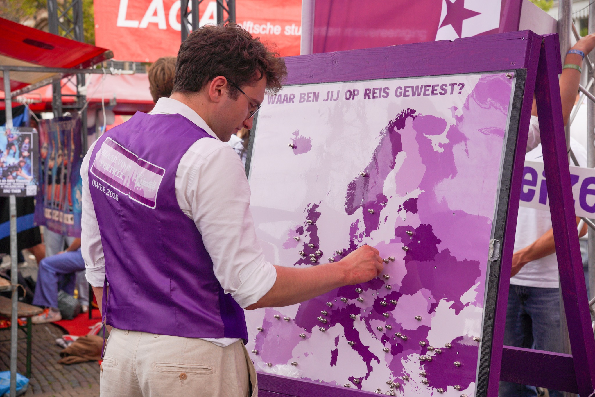 Een student in een paars gilet van AEGEE plaatst een magneet op een kaart van Europa met de tekst "Waar ben jij op reis geweest?"