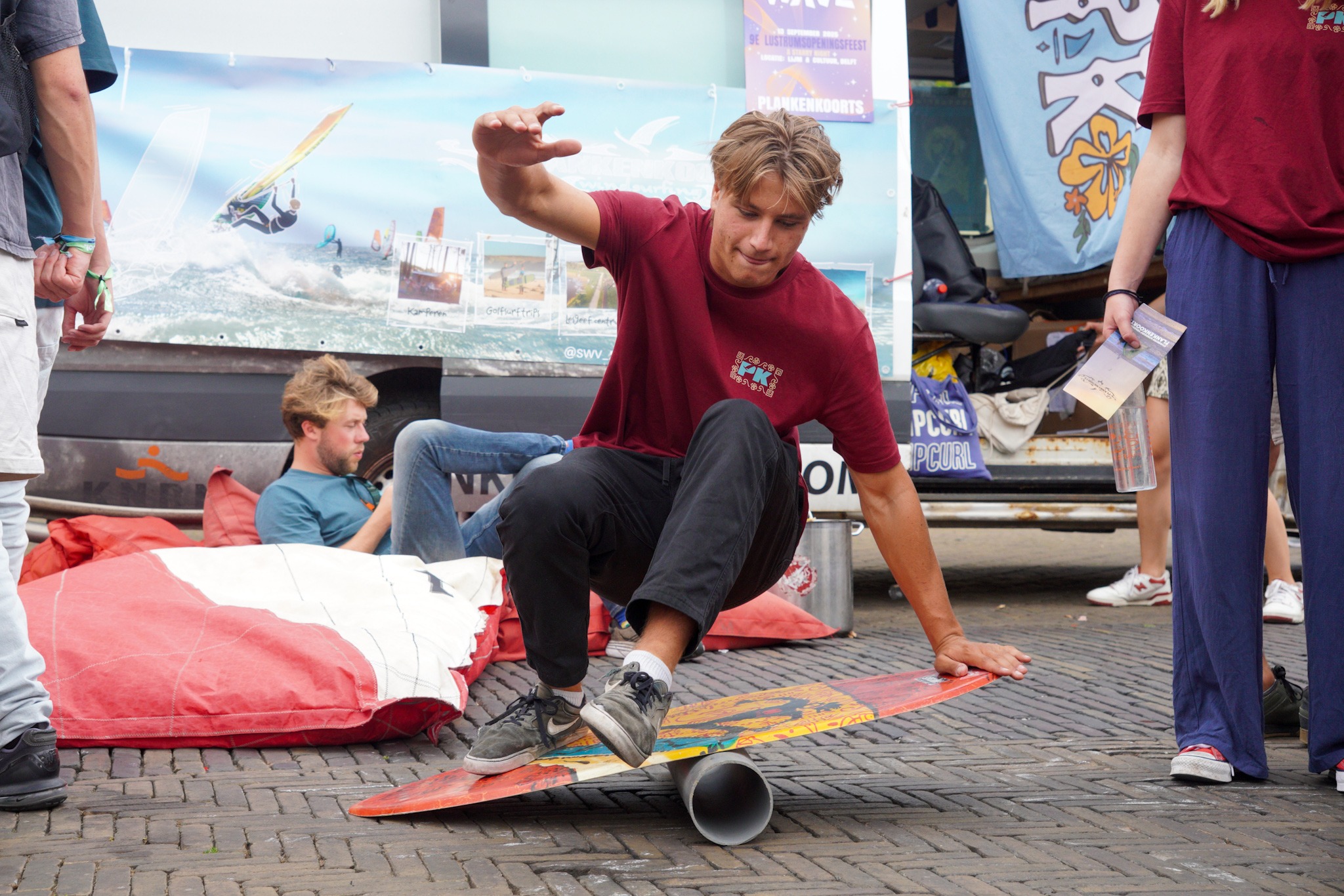 Een student met een shirt van Plankenkoorts balanceert op een kleine surfplank die op een stuk buis ligt.