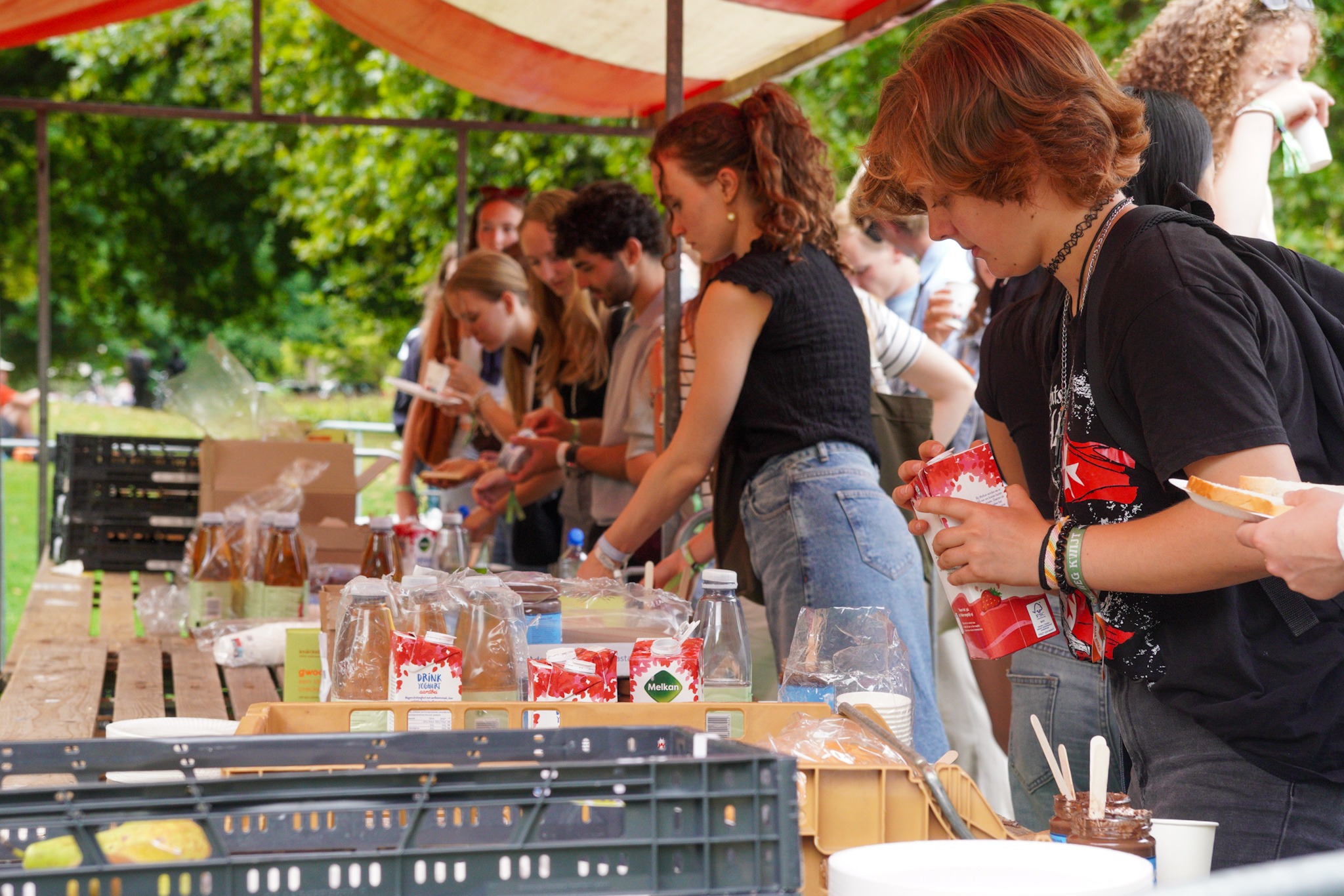Deelnemers aan de OWee staan bij een marktkraam en smeren boterhammen of schenken drinken in.