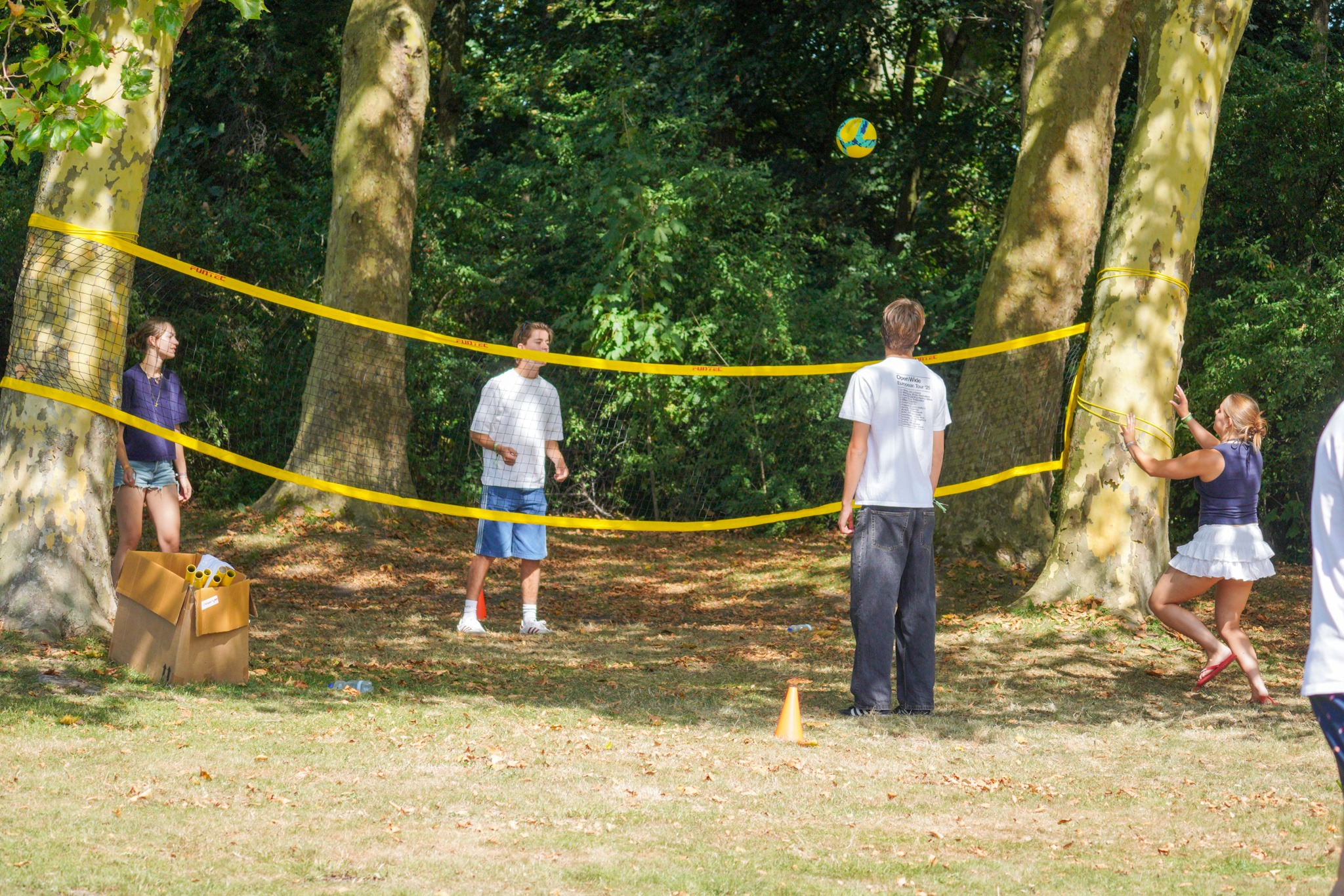 Vier deelnemers aan de OWee spelen volleybal rond een net dat tussen twee bomen is gespannen.