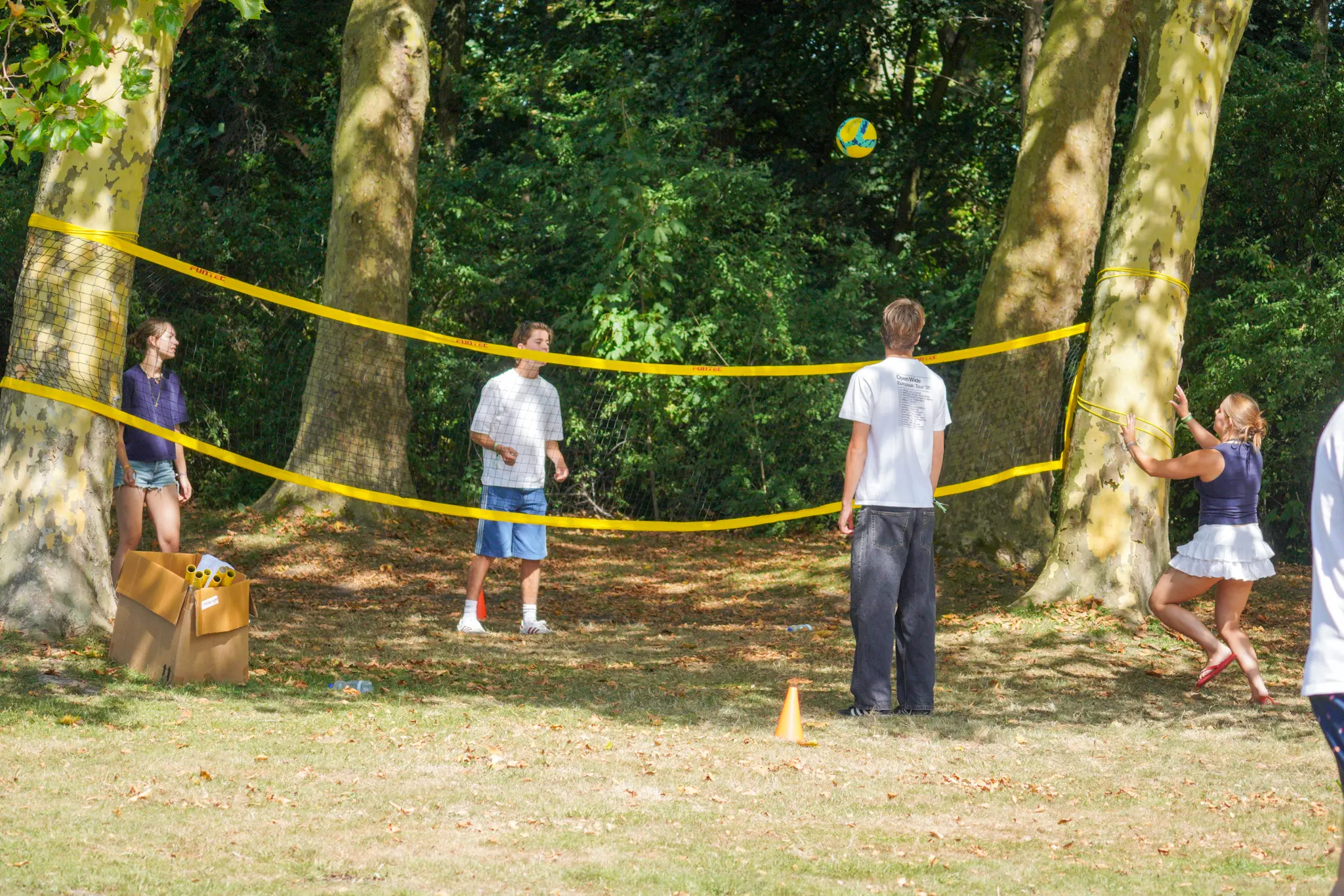 Vier deelnemers aan de OWee spelen volleybal rond een net dat tussen twee bomen is gespannen.