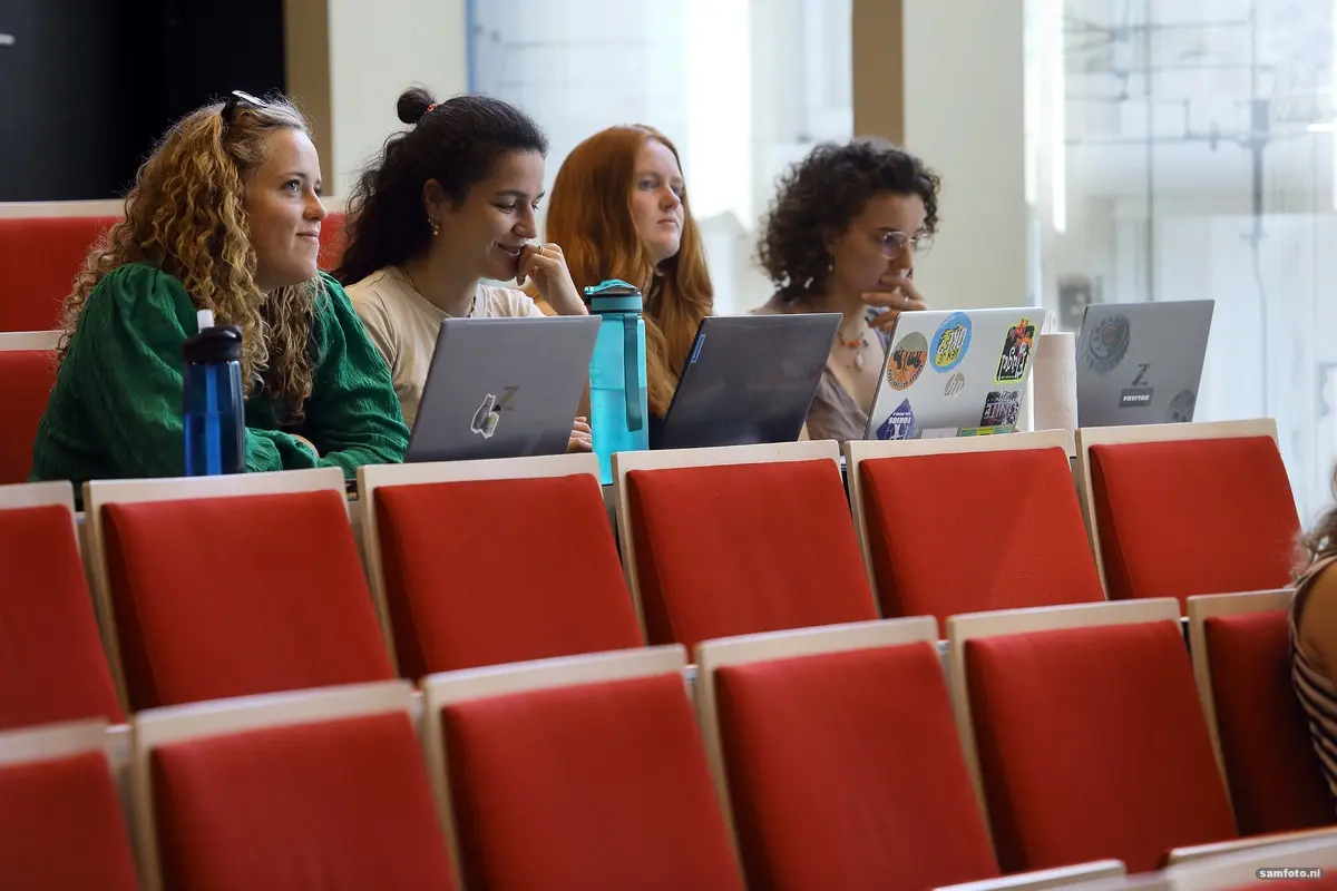 Vier studenten zitten op een rij in een collegezaal, laptops opengeklapt voor zich