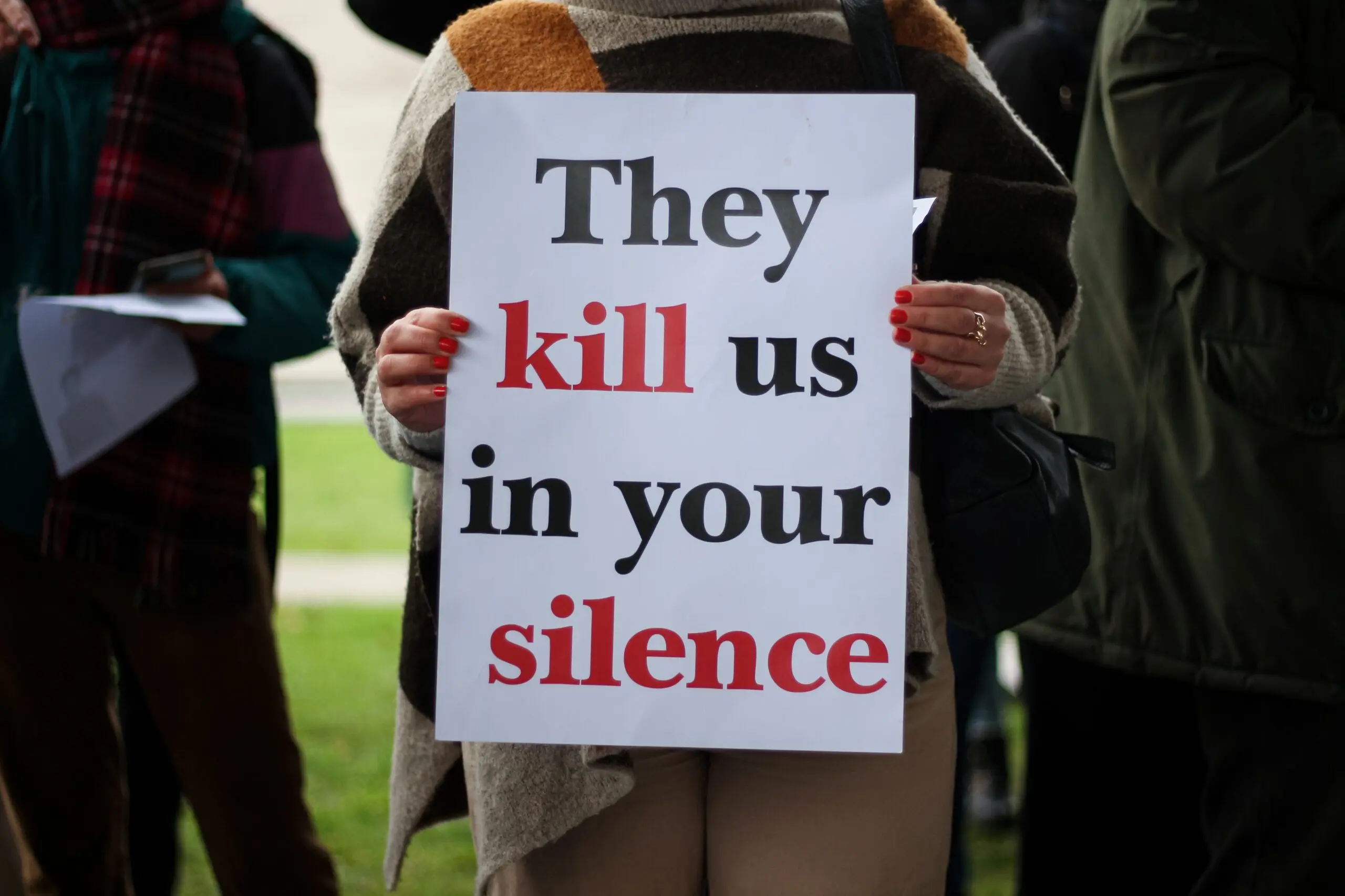 Large-scale protests at universities in Iran: ‘Courage and determination’ Iemand houdt het bord 'they kill us in your silence' vast. Haar hoofd is niet zichtbaar