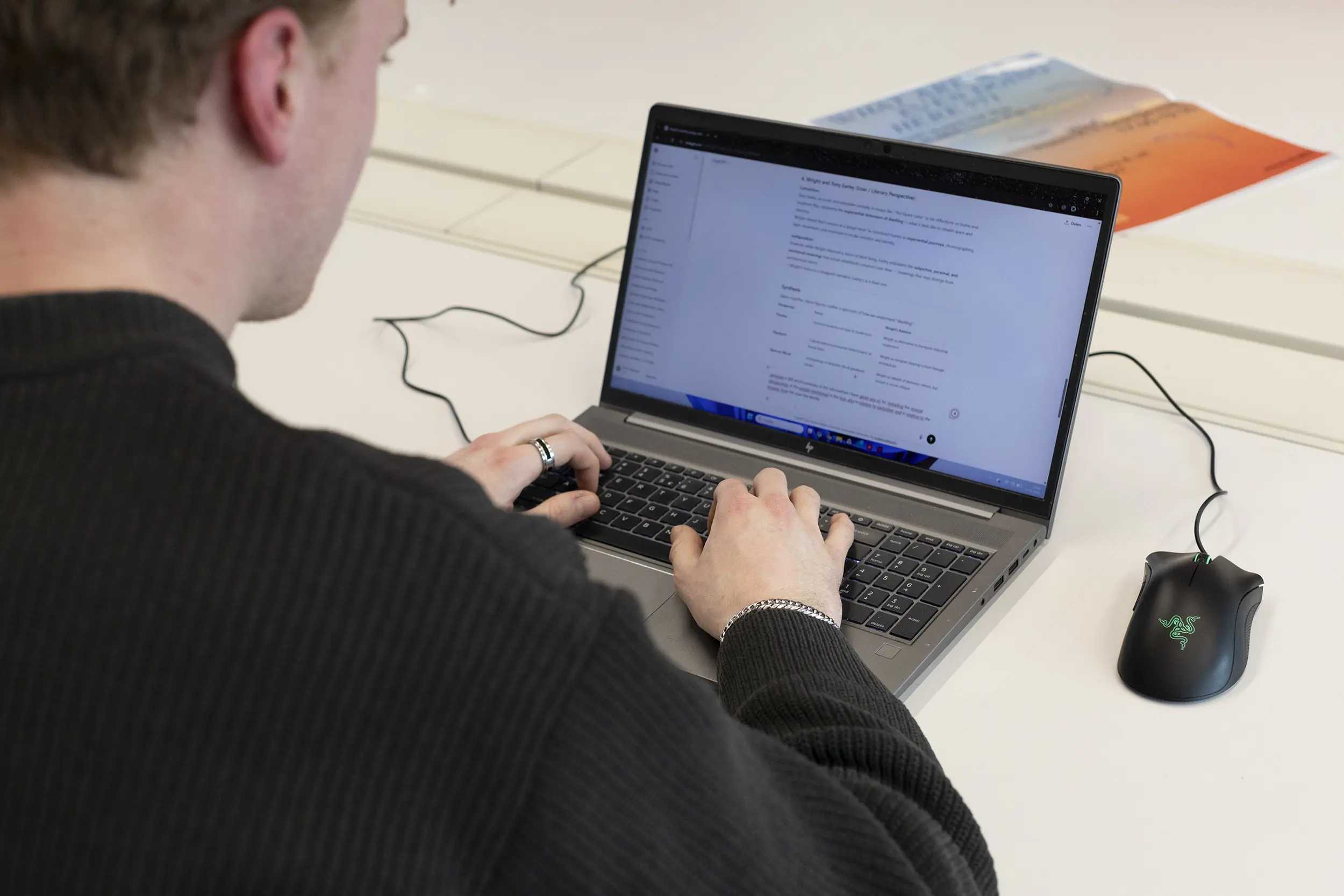 Iemand werkt op een laptop. Je ziet de persoon schuin van achteren en kijkt mee op het scherm