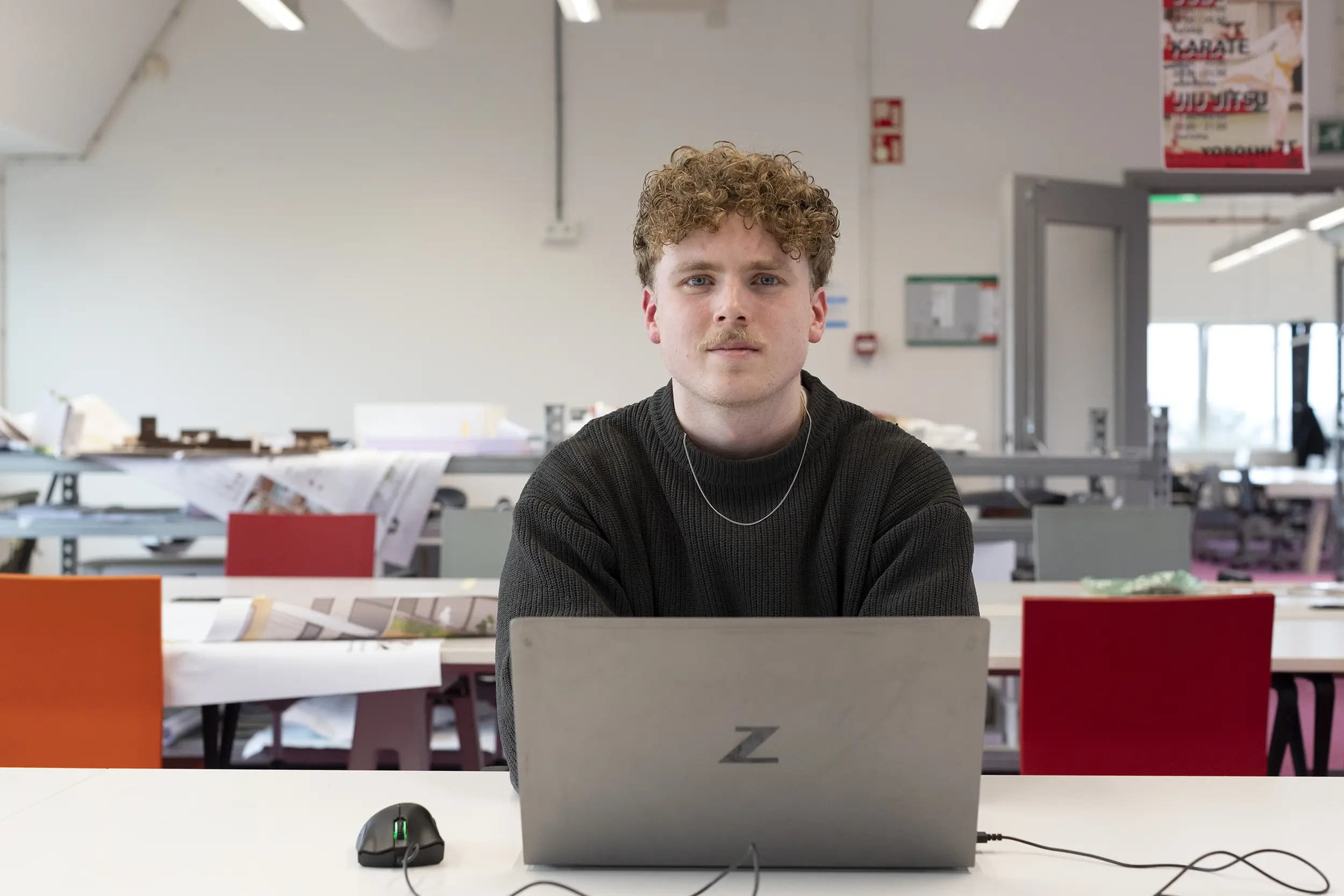 Student Bob zit achter een bureau met een laptop erop en kijkt in de camera