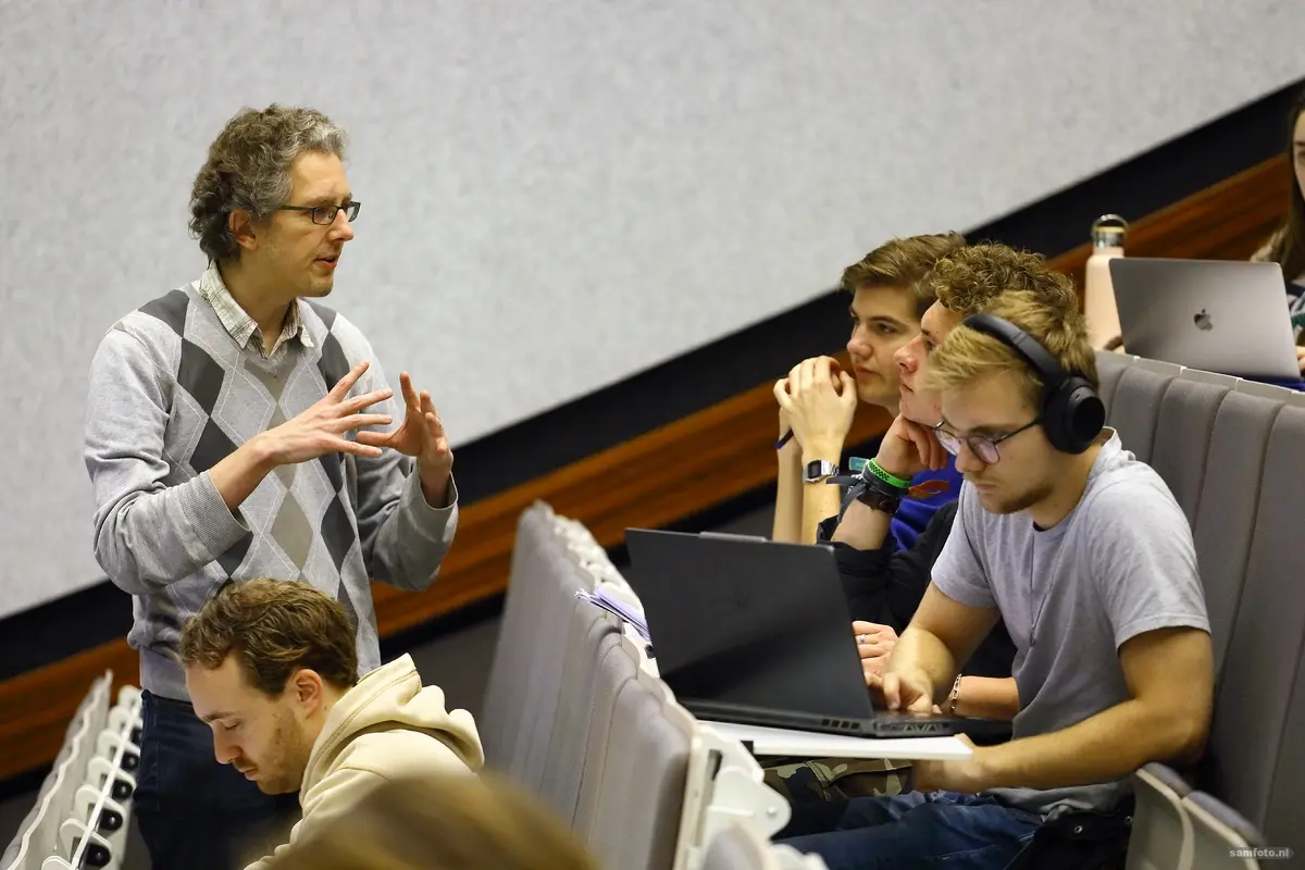 een docent staat tussen de studenten iets uit te leggen