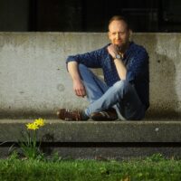 Sander Otte poseert voor de foto. Hij zit in kleermakerszit op een betonnen bankje