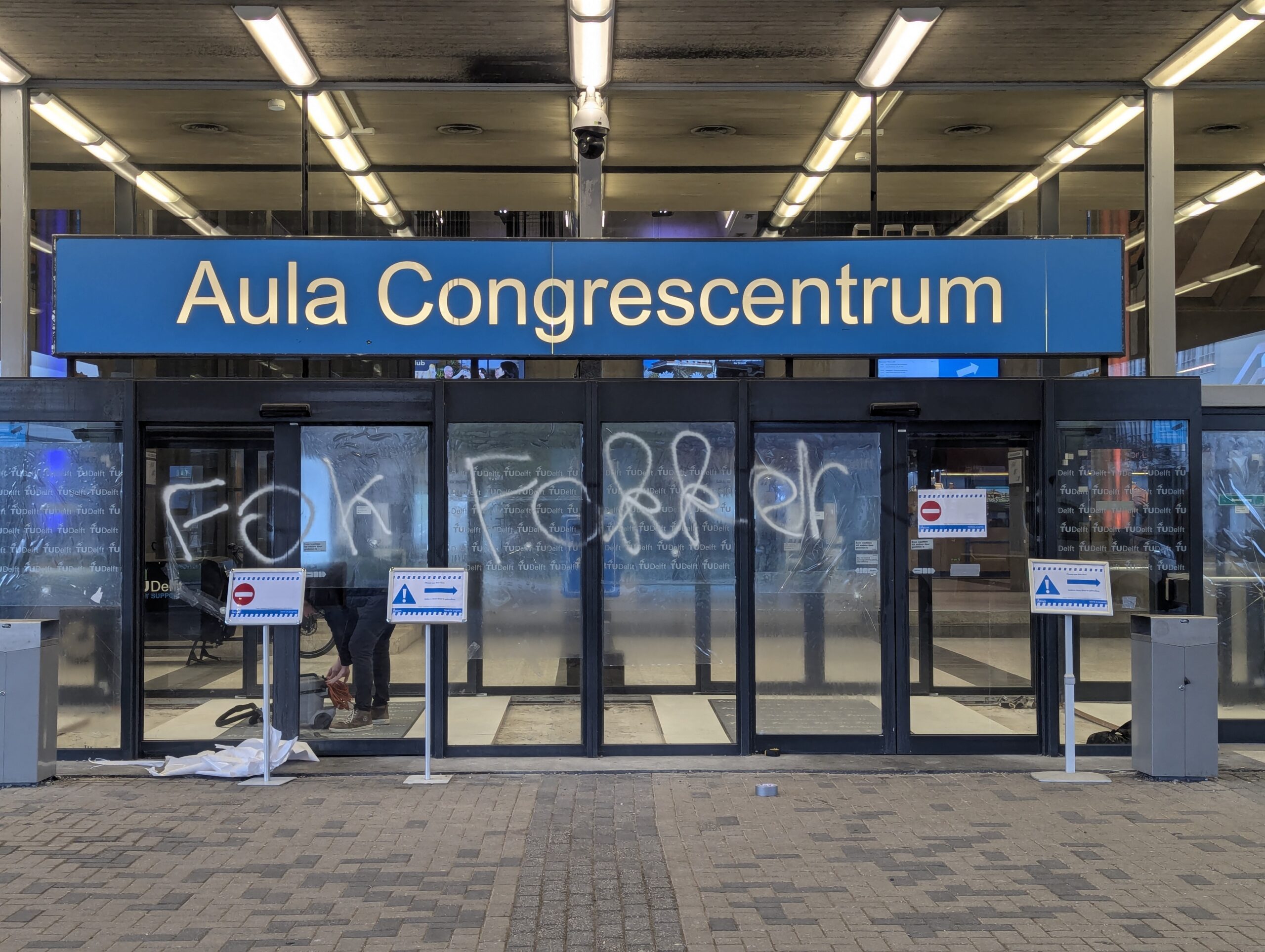 de hoofdingang van het aula congrescentrum. De deuren hebben barsten en op de ramen is Fok Fokker geklad