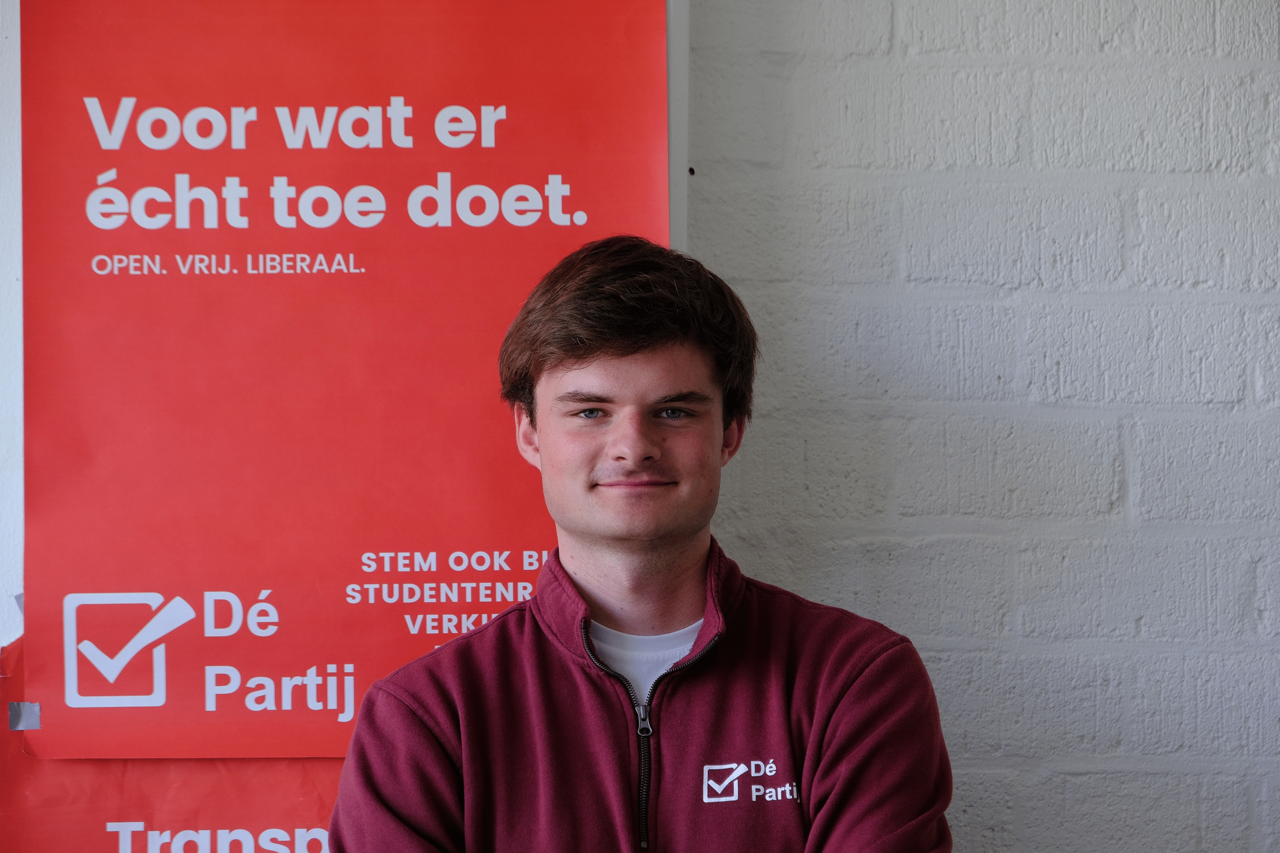 Koos Meesters poseert voor de foto met op de achtergrond een poster van De Partij.