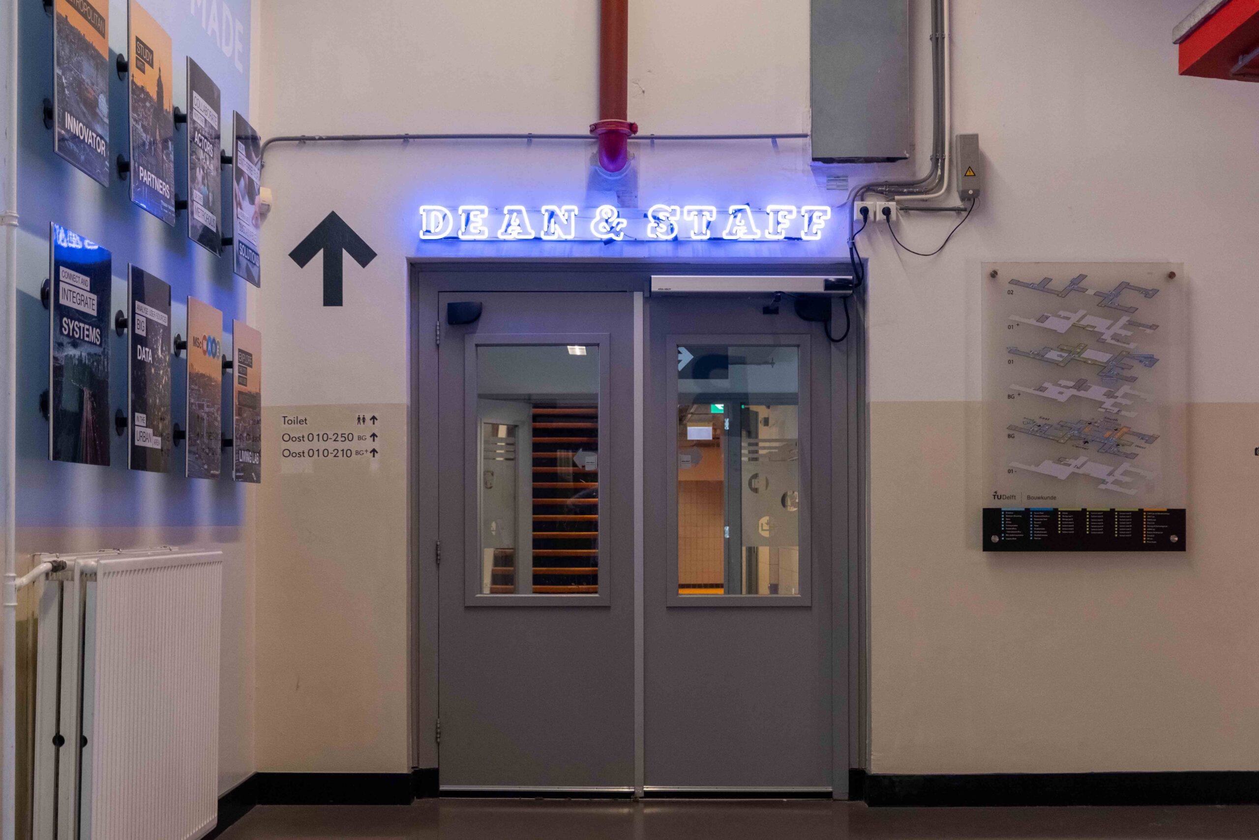 Een gang op de faculteit Bouwkunde. Te zien zijn de deuren naar de afdeling waar in neonletters boven staat: Dean & Staff