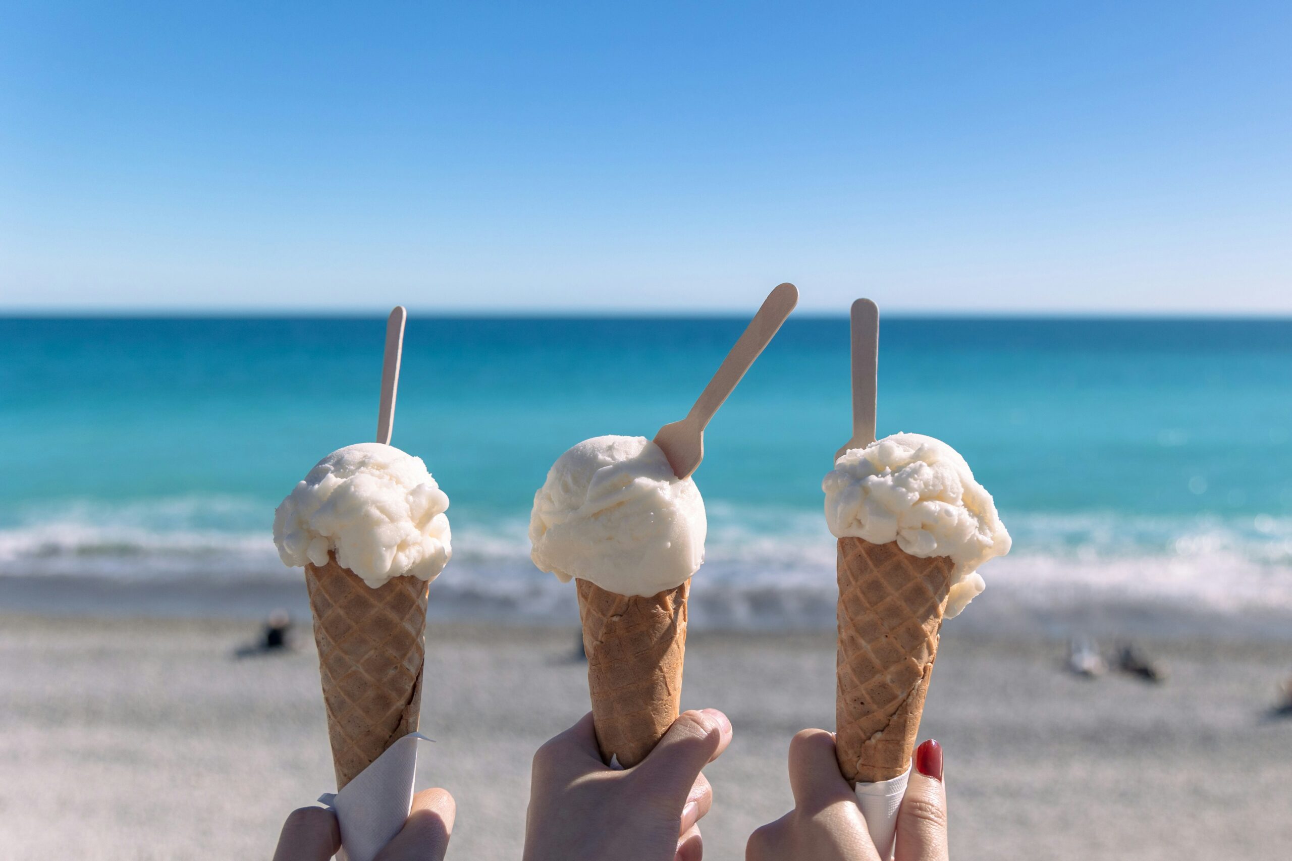 Delta is on its summer break, but you needn’t be bored Op de voorgrond drie ijsjes die omhoog worden gehouden. Op de achtergrond strand en zee.